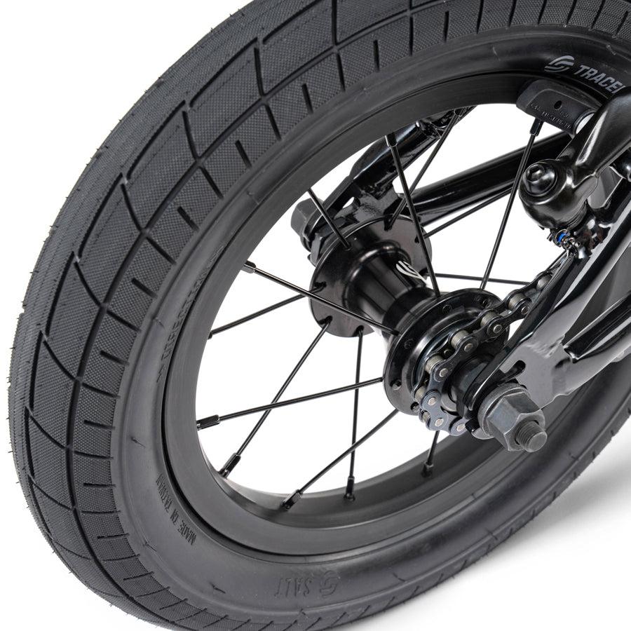 A close up of the front wheel of a black Wethepeople Prime Drive 12 Inch Bike.