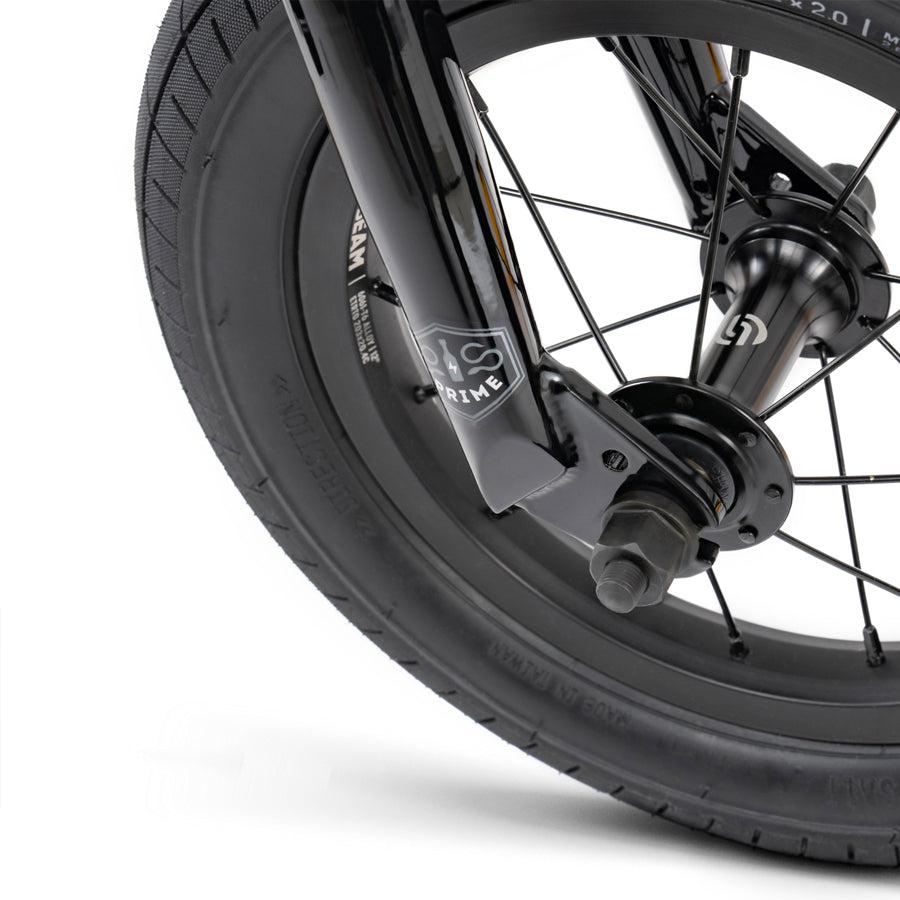 A close up of the front wheel of a black Wethepeople Prime Drive 12 Inch Bike.