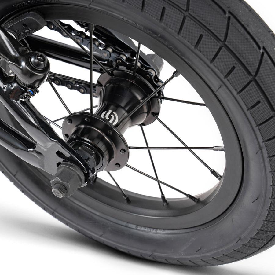 A close up of the front wheel of a black bike, featuring the Wethepeople Prime Drive 12 Inch Bike.