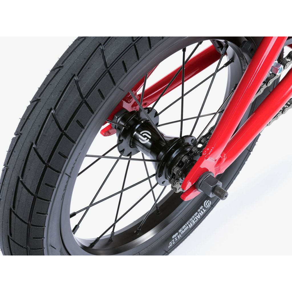 Close-up of the Wethepeople Riot 14 Inch Bike’s rear wheel, highlighting its red frame, black tire, spokes, hub, visible branding on rim and tire, plus signature style and durable Chromoly cranks.
