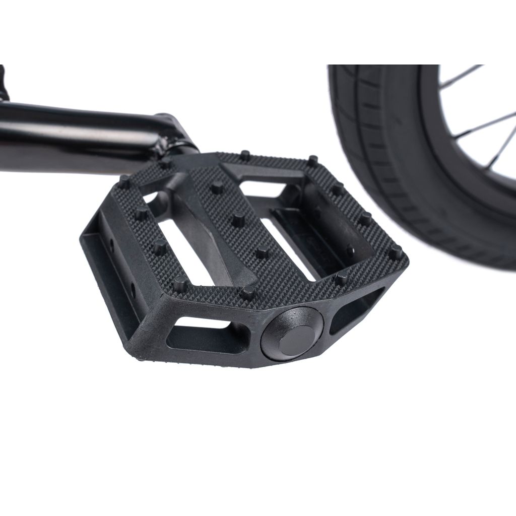 Close-up of a black bicycle pedal attached to Chromoly Cranks on a BMX, with part of the Wethepeople Riot 14 Inch Bike’s wheel visible in the background.