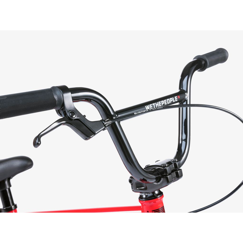 Close-up of black handlebars with grip and brake lever on a red frame. The "WETHEPEOPLE" branding is visible, featured on the Wethepeople Riot 14 Inch Bike.