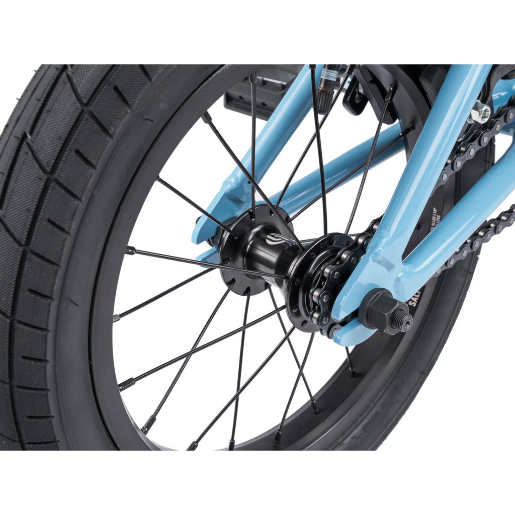 Close-up of the Wethepeople Riot 14 Inch Bike’s rear wheel, featuring black spokes, a thick tire, blue frame, and a hub with visible bolts.