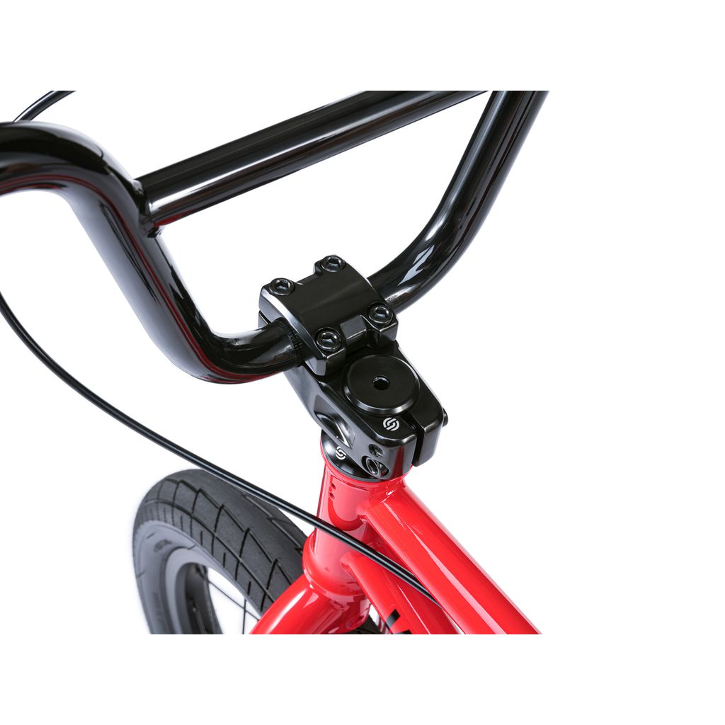 Close-up of the black handlebar and stem on the red frame of a Wethepeople Riot 14 Inch Bike, with part of the front wheel in view.