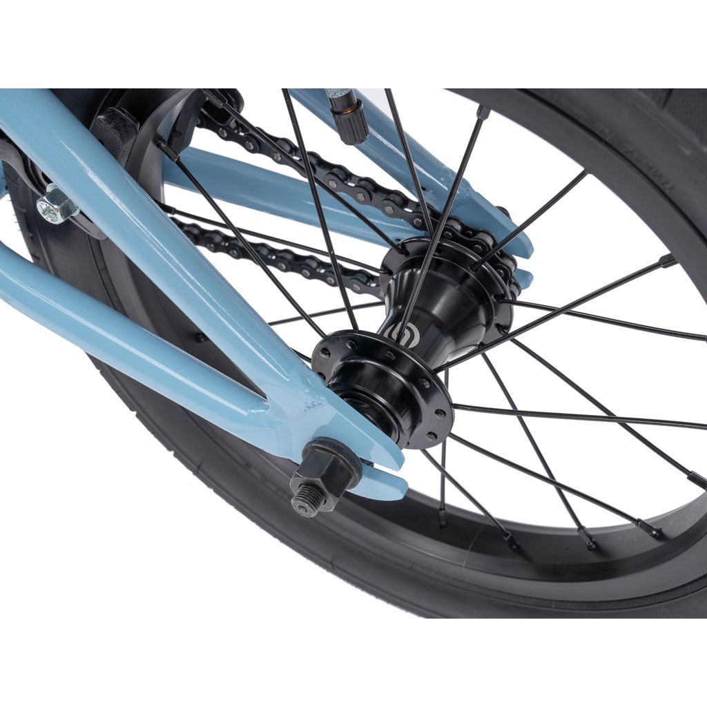Close-up of the Wethepeople Riot 14 Inch Bike’s rear wheel, featuring a blue frame, black spokes, chain, axle nut, and sturdy Chromoly cranks.