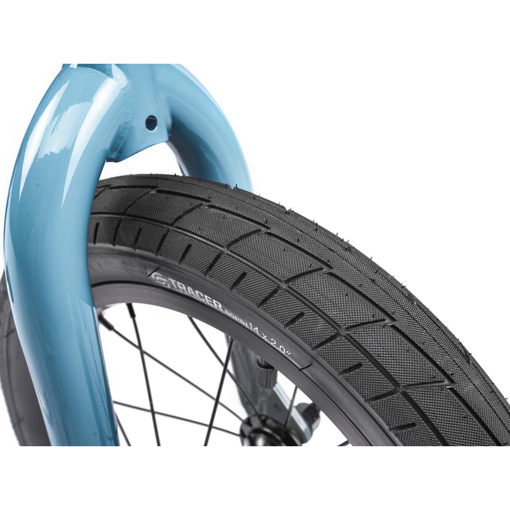 Close-up of the Wethepeople Riot 14 Inch Bike's front wheel, featuring a black, textured-tread tire with sidewall branding and a blue fork. Rugged chromoly cranks enhance durability for young BMX riders.