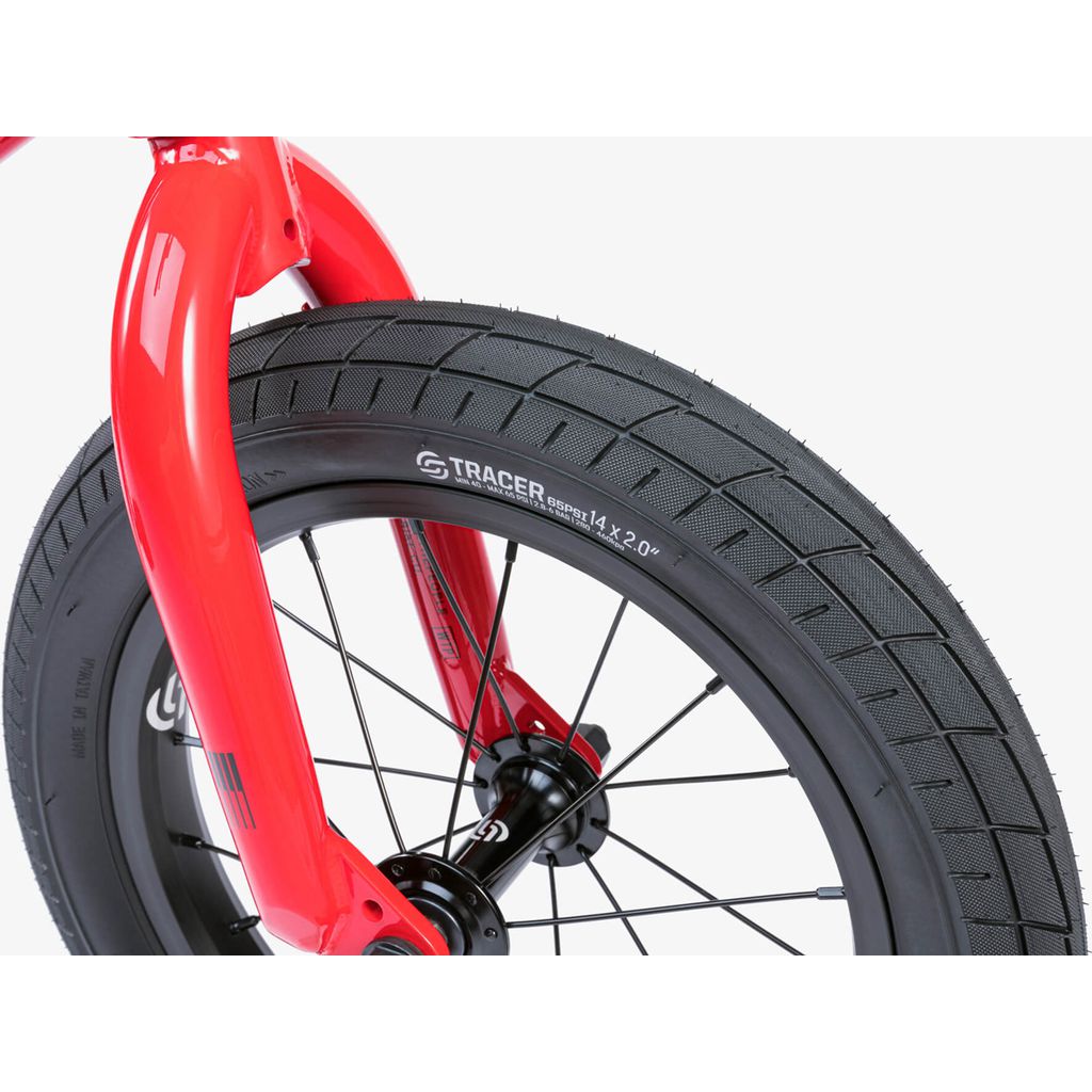 Close-up of the Wethepeople Riot 14 Inch Bike’s red BMX fork and front wheel with a G Tracer Original 14 x 2.00 tire, black spokes, and visible hub.