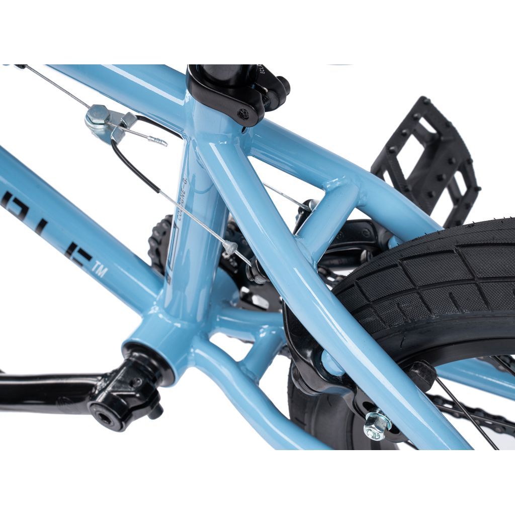 Close-up view of the Wethepeople Riot 14 Inch Bike’s blue frame, highlighting the rear triangle, brake cable, rear tire, pedal, and chainstay details.