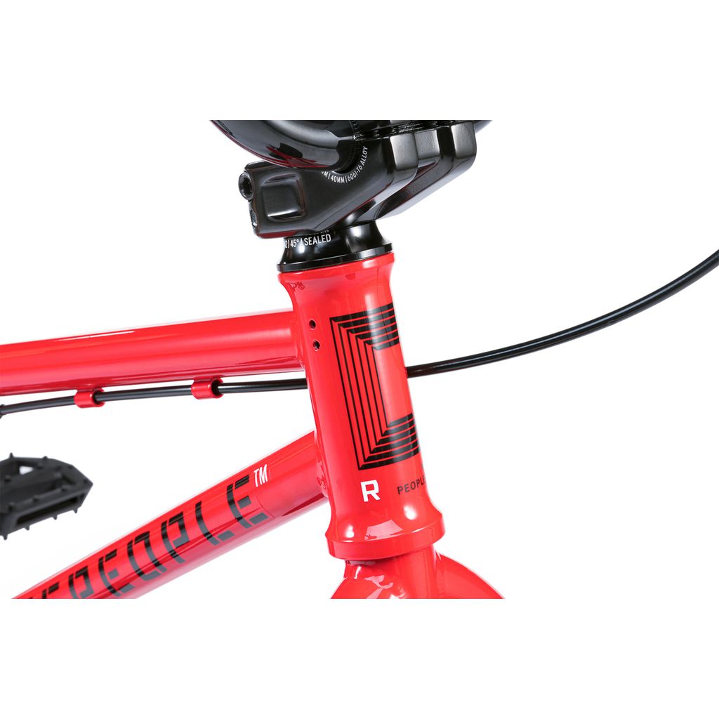 Close-up of a Wethepeople Riot 14 Inch Bike's red front frame and handlebars, featuring geometric black detailing, Chromoly Cranks, and visible brake cables.