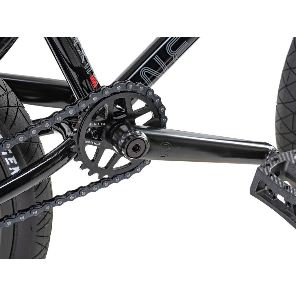 Close-up view of the Wethepeople Sinus Flatland 20 Inch Bike's black crankset, chainring, chain, hybrid freecoaster hub, and pedal connected to the frame and rear wheel.