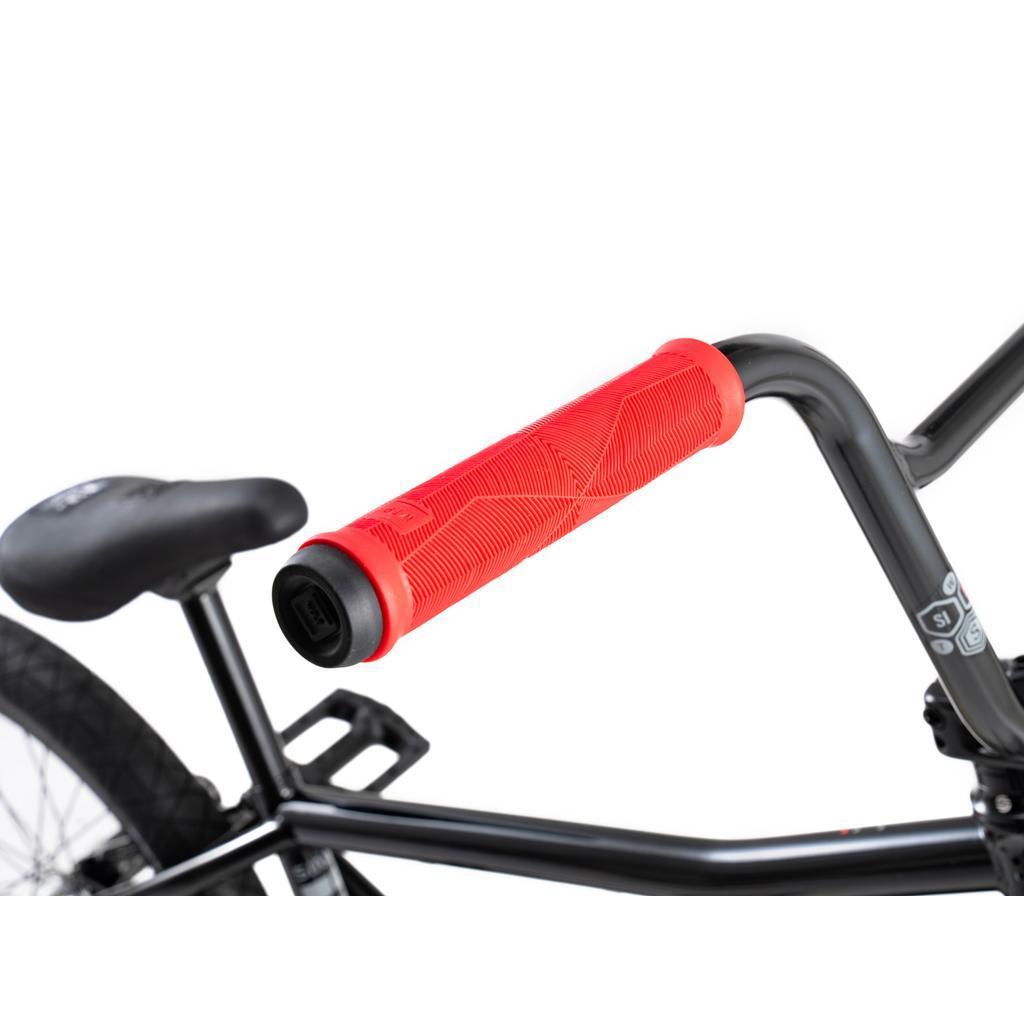 Close-up of the Wethepeople Sinus Flatland 20 Inch Bike handlebar with a red grip, black frame, and part of the seat and pedal visible against a white background, featuring flatland-specific Mugen tires.