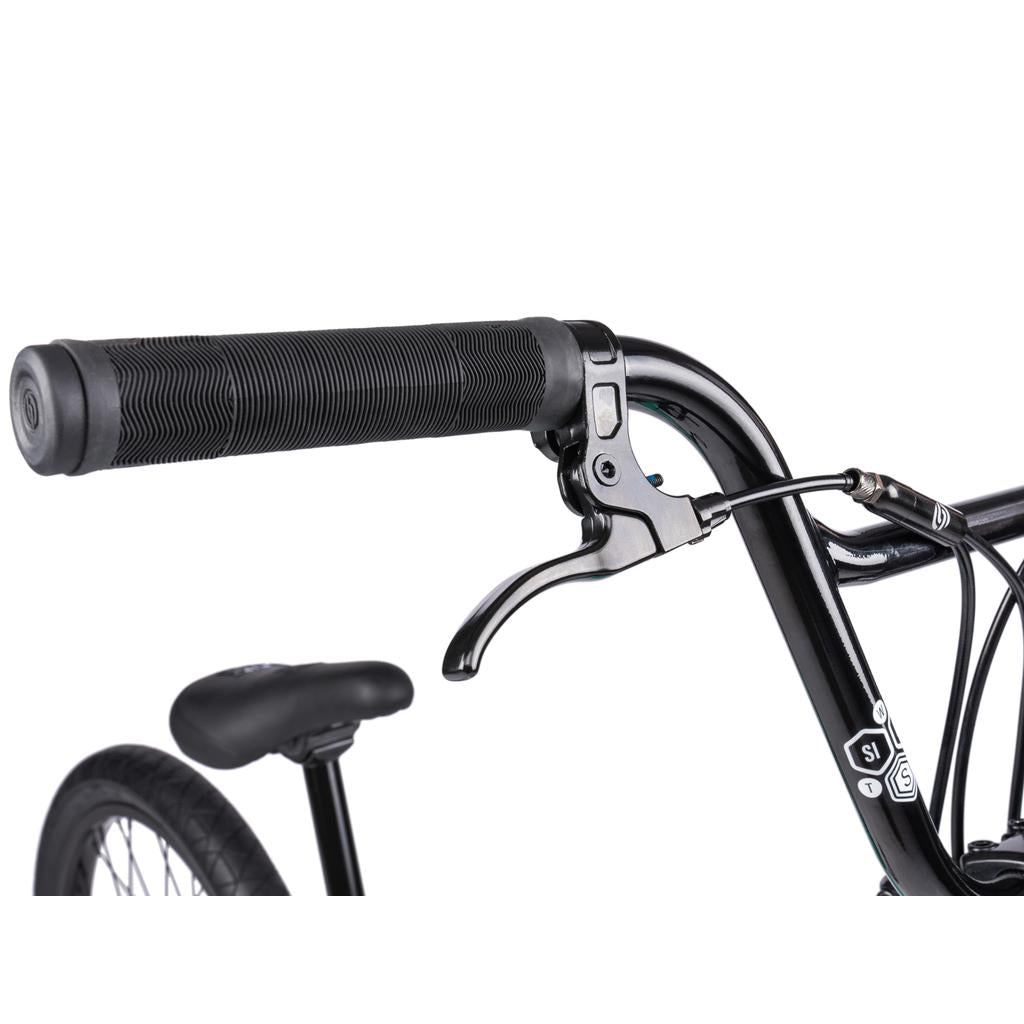 Close-up of a Wethepeople Sinus Flatland 20 Inch Bike handlebar with brake lever, rubber grip, and visible seat and flatland-specific Mugen tire in the background.