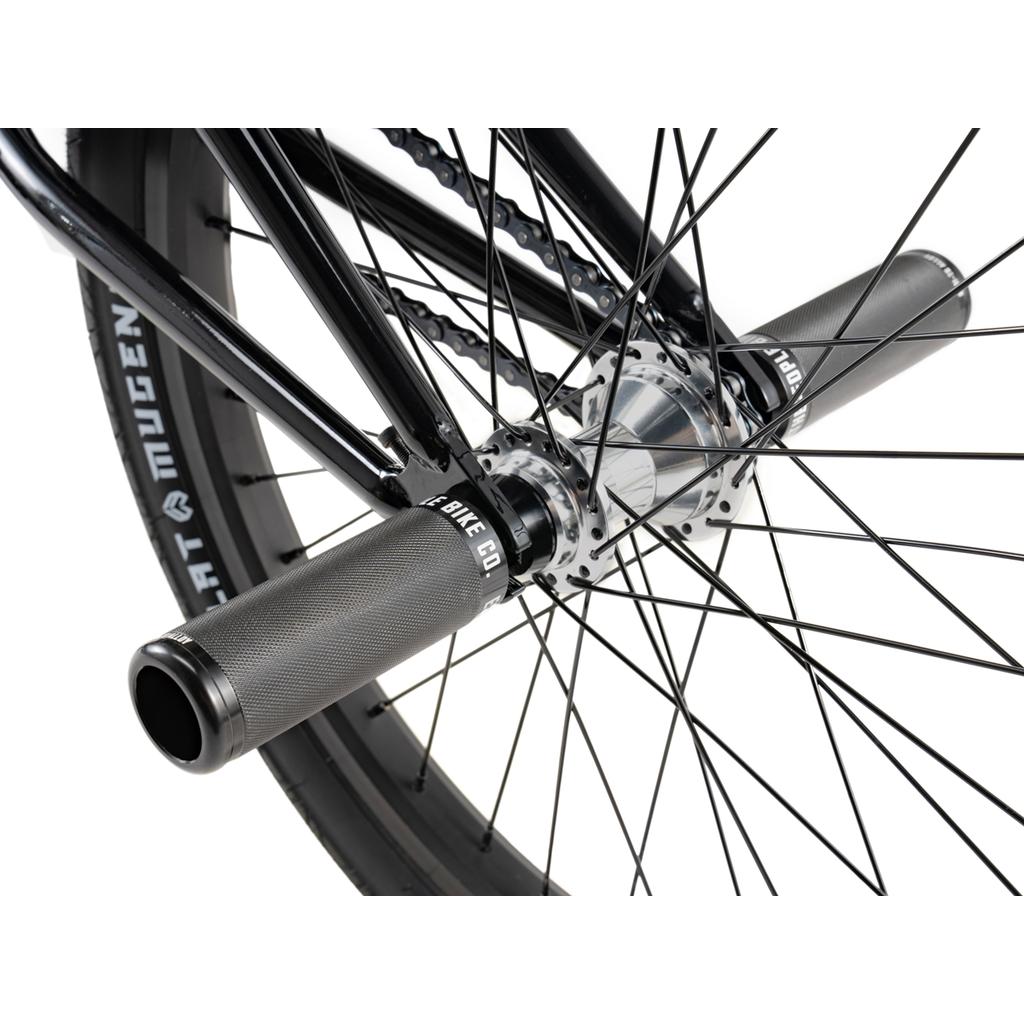 Close-up of the Wethepeople Sinus Flatland 20 Inch Bike’s rear wheel with metal pegs, chain, spokes, and a "MUGEN" tire—showcasing aftermarket parts designed for enhanced flatland BMX performance.