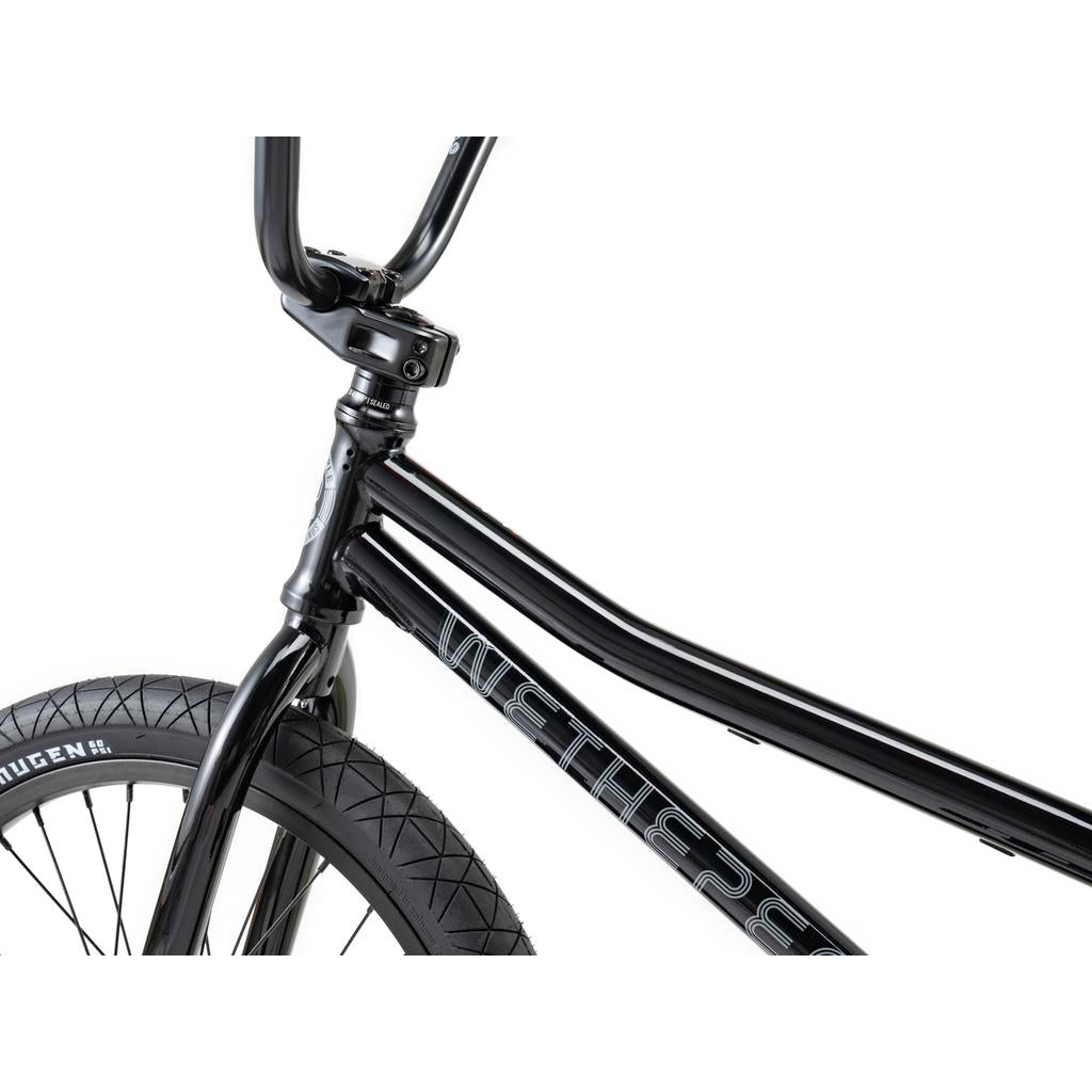 Close-up of the Wethepeople Sinus Flatland 20 Inch Bike, featuring black handlebars, a frame with the "WETHEPEOPLE" logo, and a front wheel fitted with flatland-specific Mugen tires with a "QUEEN" label, all set against a white background.