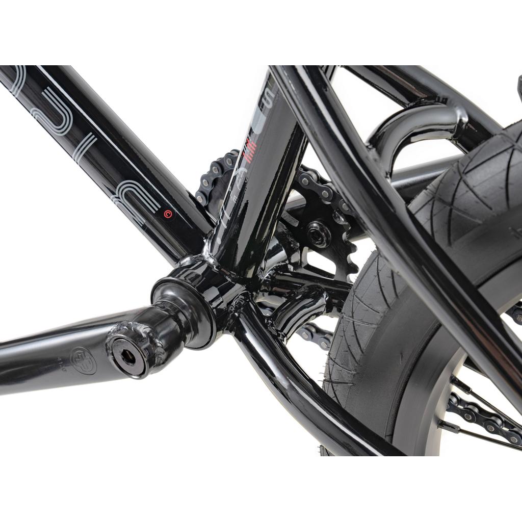 Close-up of the Wethepeople Sinus Flatland 20 Inch Bike frame, highlighting the crank, chainring, and rear tire details, aftermarket metal components, and tread pattern.