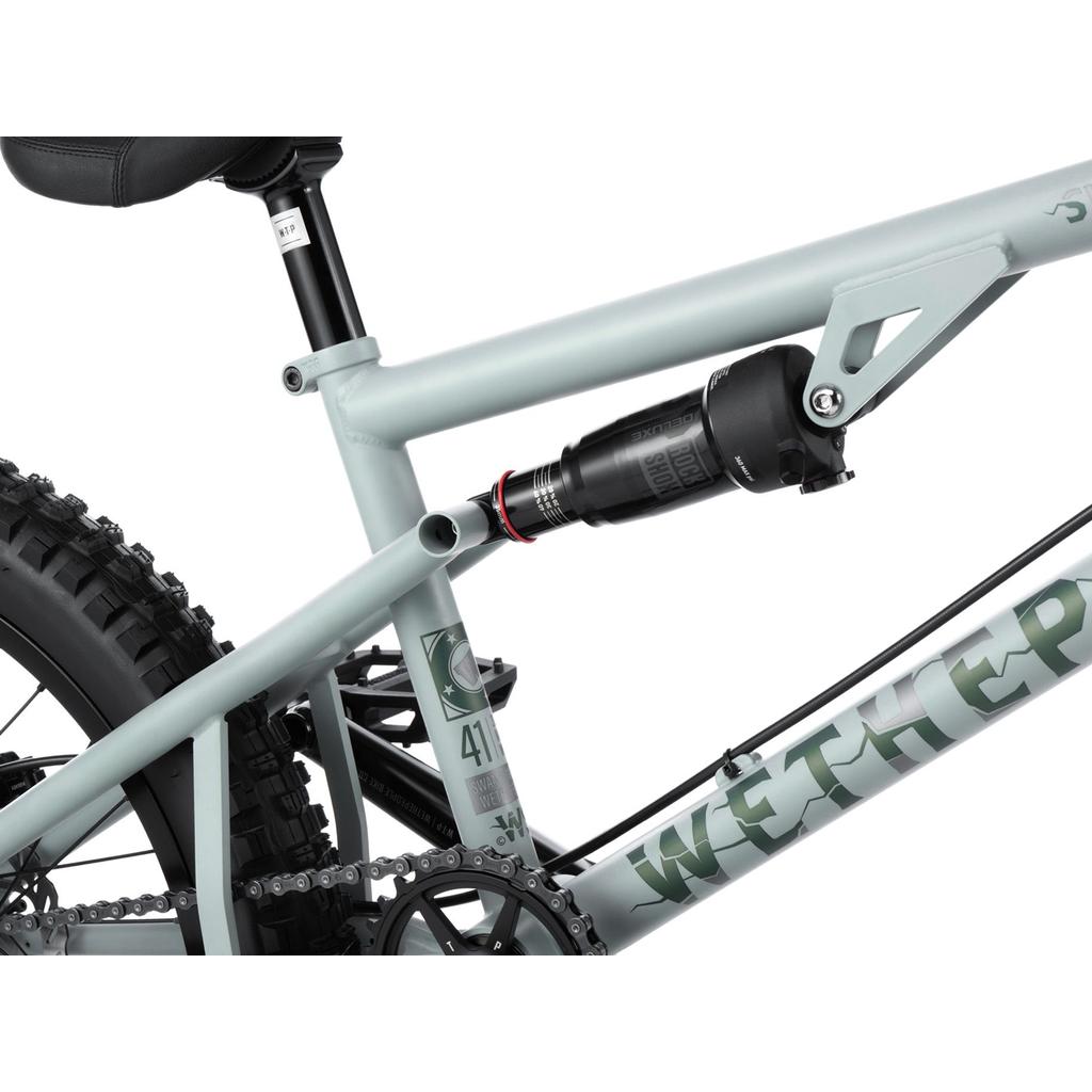 Close-up of the Wethepeople Swampmaster 20 Inch Bike frame in light gray, featuring full suspension with a rear shock absorber and part of the drivetrain, designed for downhill mountain biking and select BMX components compatibility.