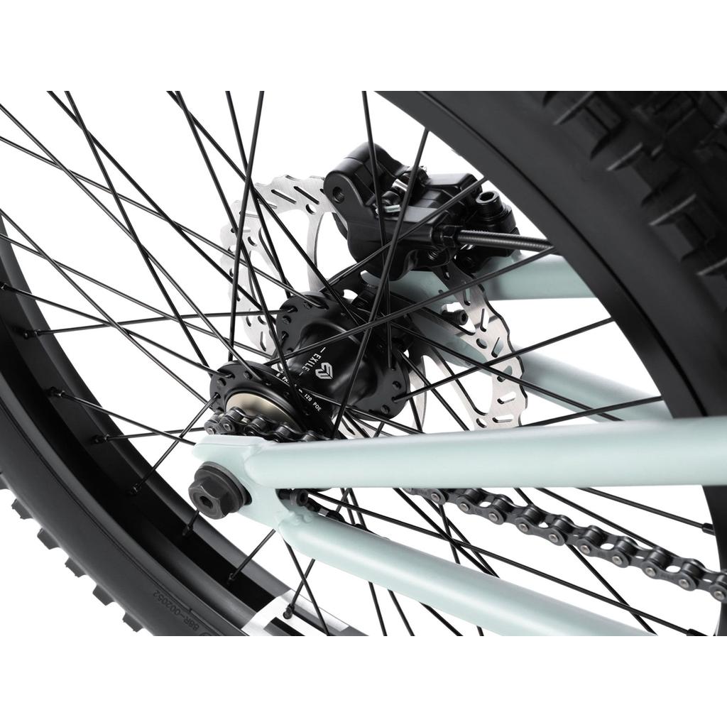 Close-up of the Wethepeople Swampmaster 20 Inch Bike's rear wheel, featuring the disc brake, rotor, chain, axle, and spokes on its light blue BMX frame.