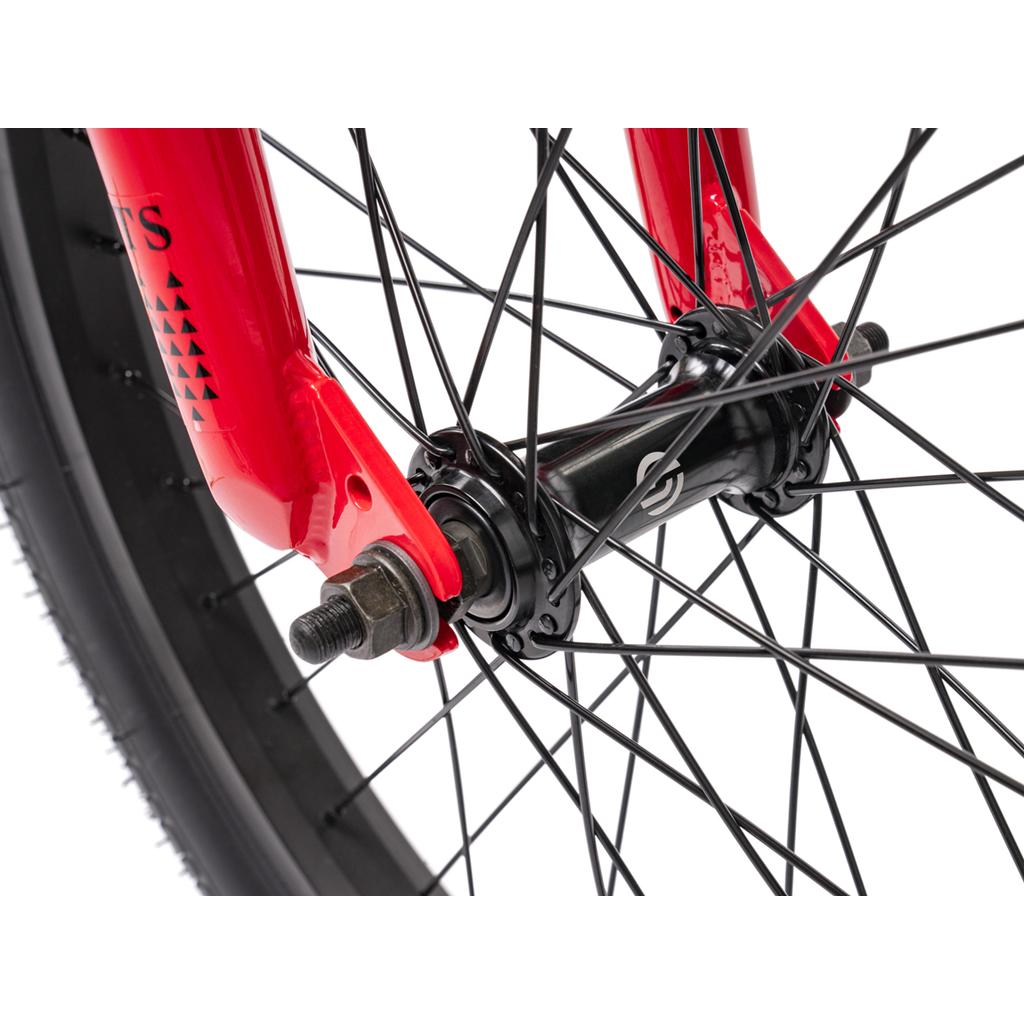 Close-up of the Wethepeople Thrillseeker 20 Inch Bike’s front wheel with black spokes, red fork, and axle with nuts against a white background, highlighting its connection to the Hi-Ten frame.