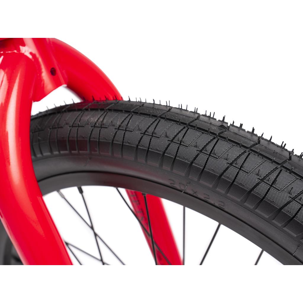 Close-up of a black-treaded bicycle tire mounted on a red Wethepeople Thrillseeker 20 Inch Bike frame, shown against a white background.