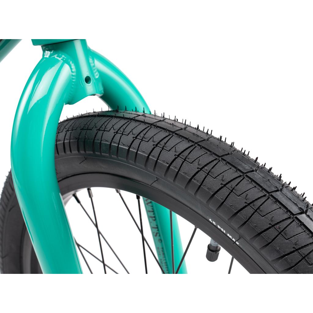 Close-up of the front wheel and tire on the Wethepeople Thrillseeker 20 Inch Bike, featuring a turquoise frame, detailed tread pattern, black spokes, and signature Salt Thrillseeker handlebars.
