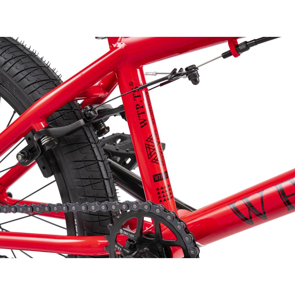 Close-up of the Wethepeople Thrillseeker 20 Inch Bike, a red freestyle BMX with a Hi-Ten frame, showing chain, rear wheel, brake cable, and decals featuring "WTP" and geometric designs.