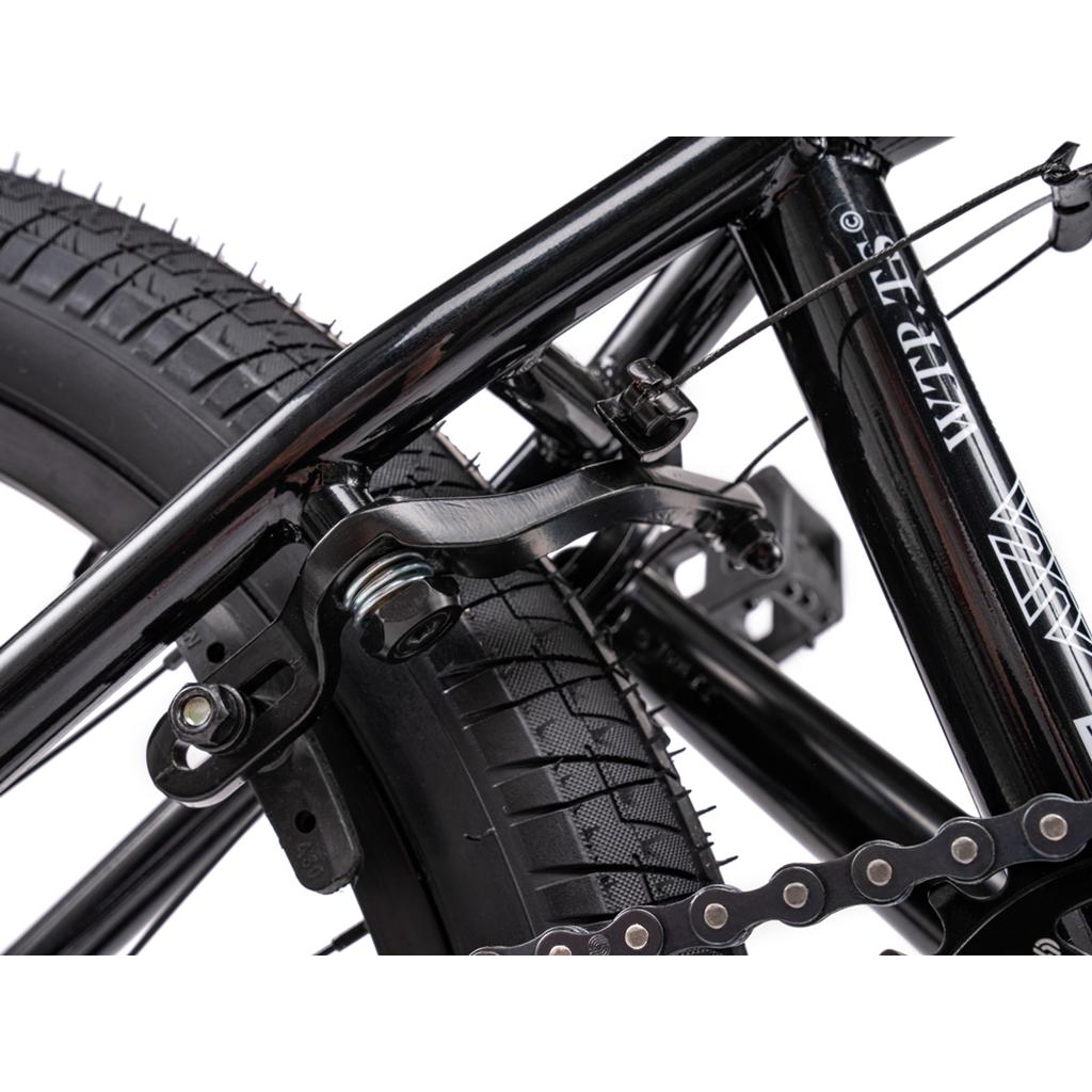 Close-up of a Wethepeople Thrillseeker 20 Inch Bike’s rear wheel, showcasing the brake mechanism, tire tread, chain, and durable Hi-Ten frame components.