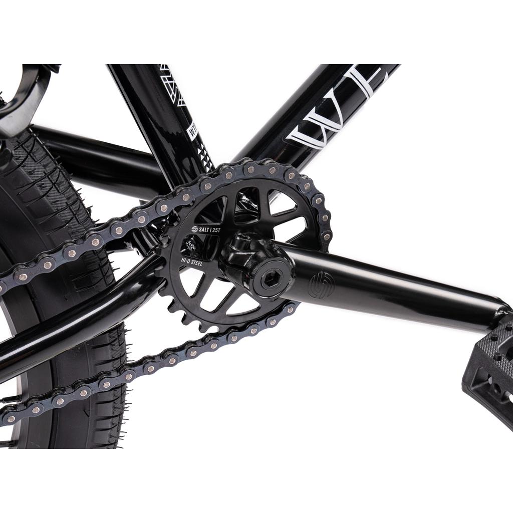 Close-up view of a black Wethepeople Thrillseeker 20 Inch Bike crankset, chainring, and pedal, highlighting the tire tread, chain detail, and bold Salt Thrillseeker handlebars.