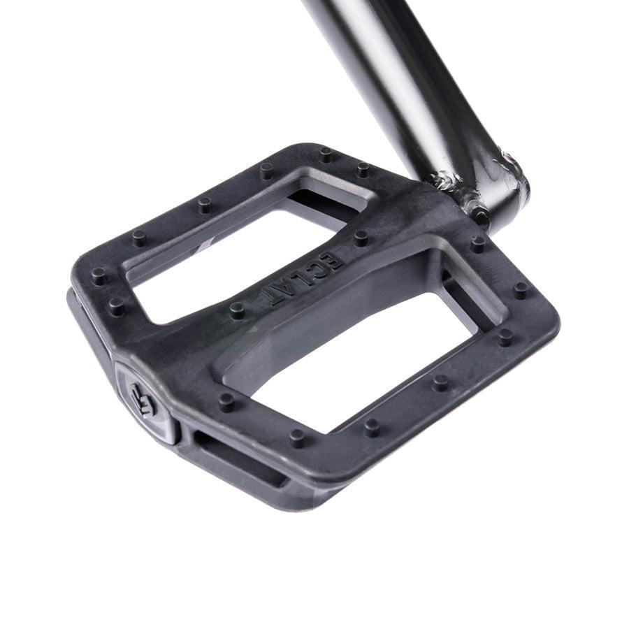 Close-up of a black bicycle pedal with a rectangular, flat design and raised traction pins attached to a crank arm on a Wethepeople Trust 20 Inch Cassette/Hybrid Bike.