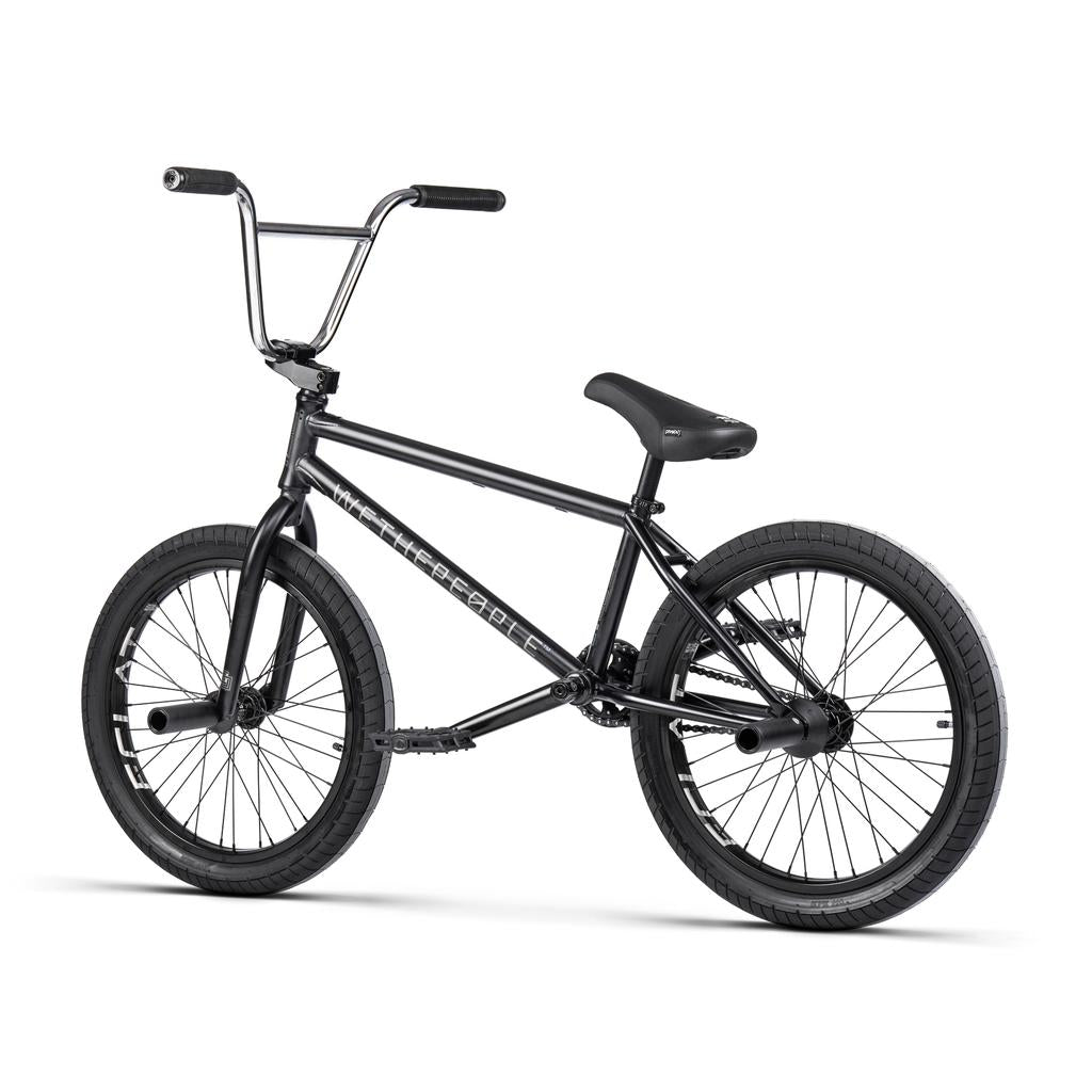 A black Wethepeople Trust 20 Inch Cassette/Hybrid Bike with a straight handlebar, padded seat, Eclat Shift Freecoaster Hub, and thick tires is displayed on a white background.