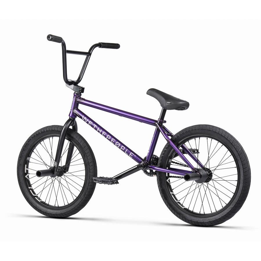 A purple Wethepeople Trust 20 Inch Cassette/Hybrid Bike with black handlebars, seat, and tires is displayed on a white background. The frame shows "WETHEPEOPLE" branding and features an Eclat Shift Freecoaster Hub for smooth rides.