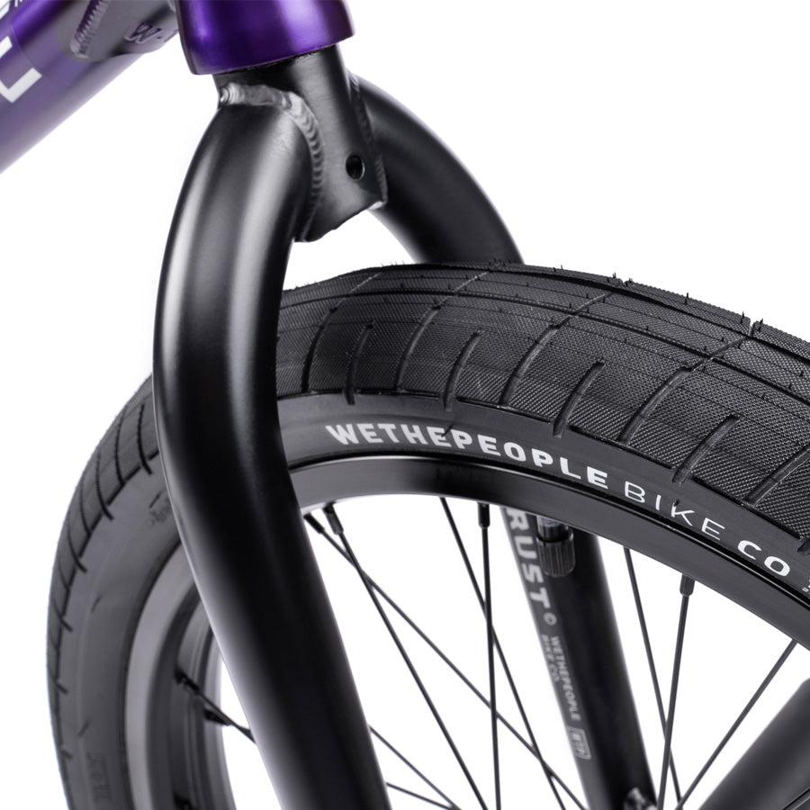 Close-up of a Wethepeople Trust 20 Inch Cassette/Hybrid Bike's front wheel with black tire, "WETHEPEOPLE BIKE CO." branding, and black fork against a white background—highlighting the bike's quality.