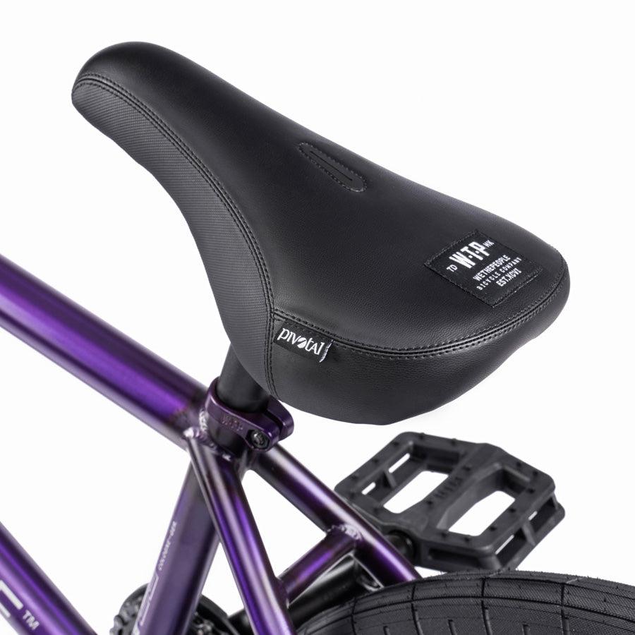 Close-up of a black bicycle seat on the purple frame of a Wethepeople Trust 20 Inch Freecoaster/Hybrid Bike, with a logo tag visible on the side.
