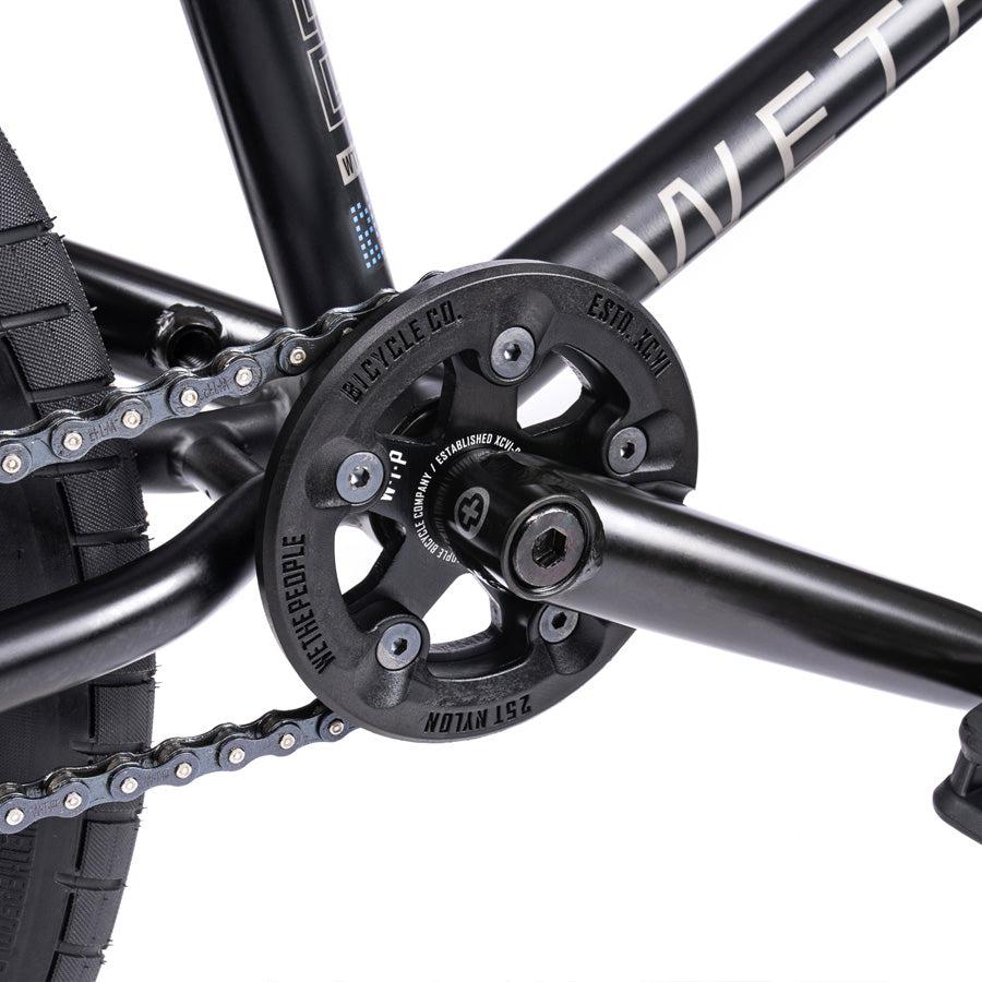 Close-up of the Wethepeople Trust 20 Inch Freecoaster/Hybrid Bike's drivetrain featuring a chain, pedal, and branded sprocket on the crank, highlighting its unique battleship geometry.