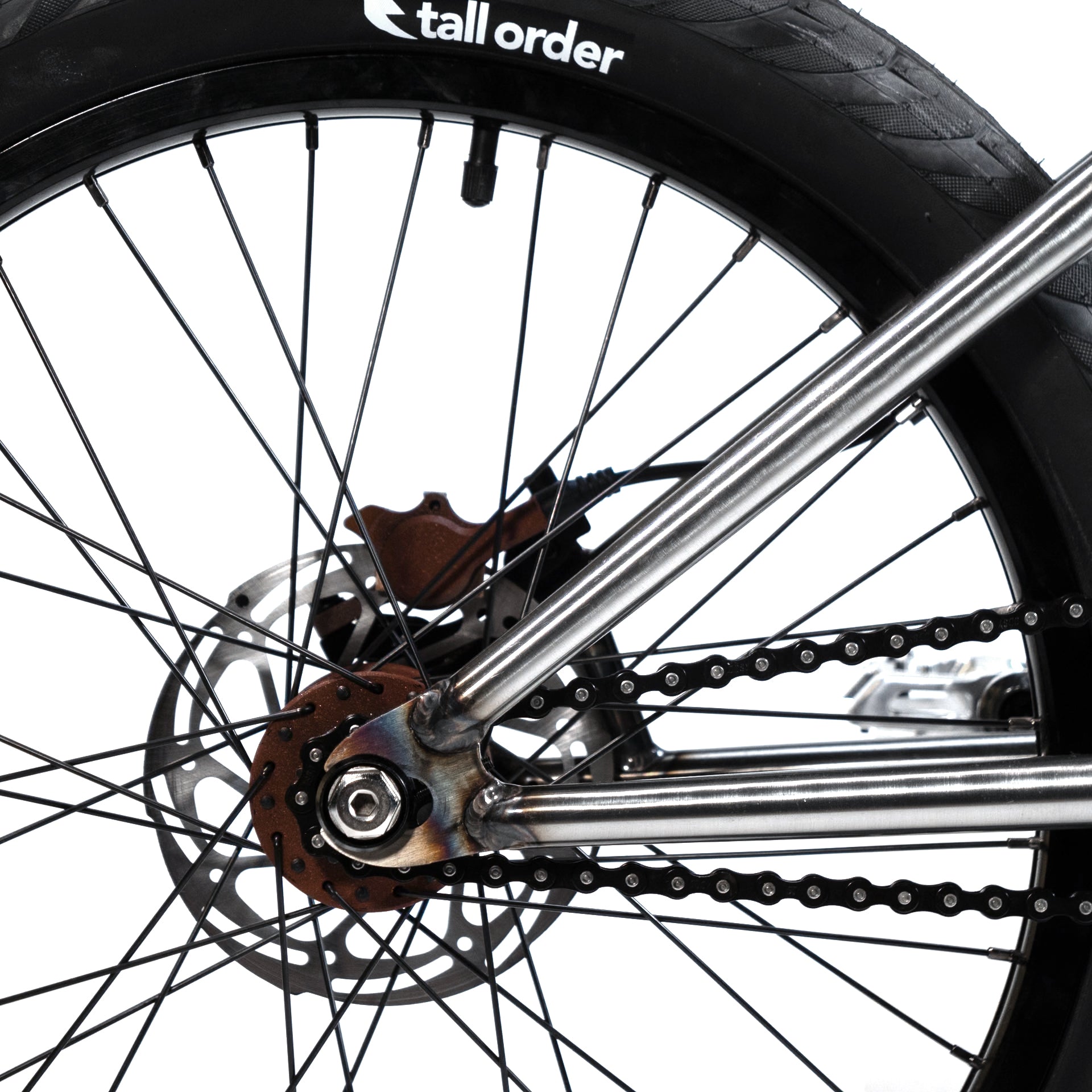 Close-up of a Wethepeople X LUX LAB 'Ironhide' Chaos Machine 20 Inch Custom Bike's rear wheel showing the tire, disc brake, chain, and metal frame against a white background.