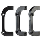 Three views of the Promax PM for IS Disc Brake Adaptor, a black aluminum alloy adapter for Post Mount disc brake calipers, featuring two bolt holes on each end, engraved markings, and compatibility with 140mm rotors.