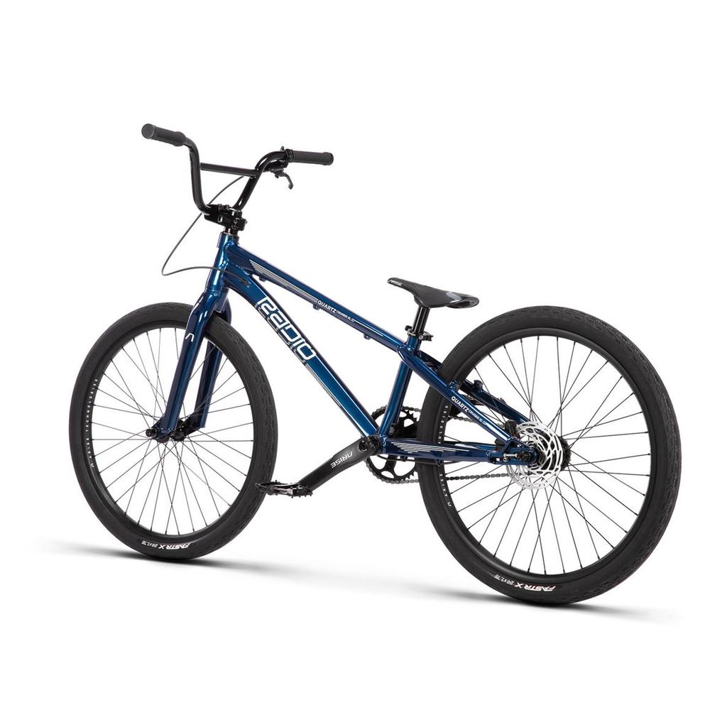The Radio Raceline Quartz Pro Disc 24 Inch Bike, featuring race-ready geometry, a lightweight blue frame, black handlebars, two large wheels, and disc brakes, is shown on a white background.