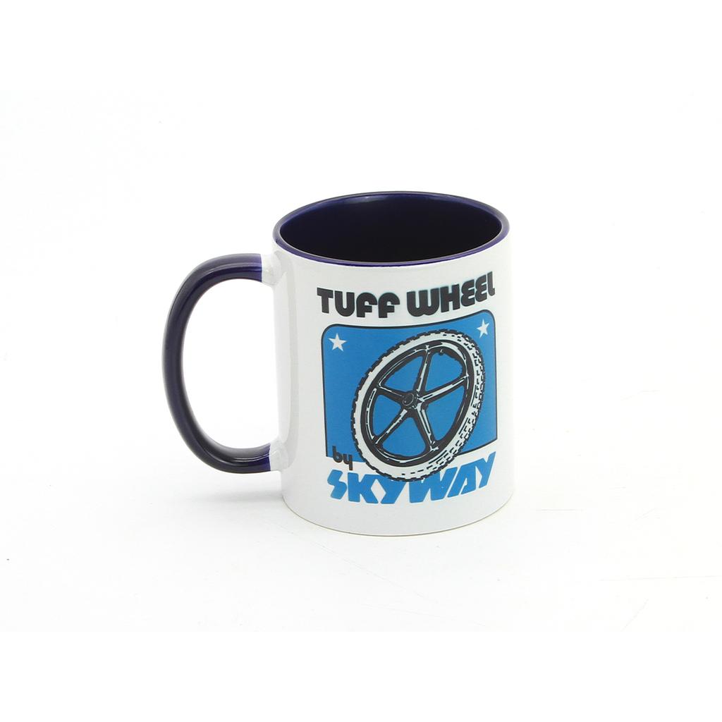 The Skyway Tuff Wheel Coffee Mug is a 12 oz white ceramic mug with a dark handle, featuring a blue bicycle wheel graphic and "TUFF WHEEL by SKYWAY" on the front—ideal for cycling fans.