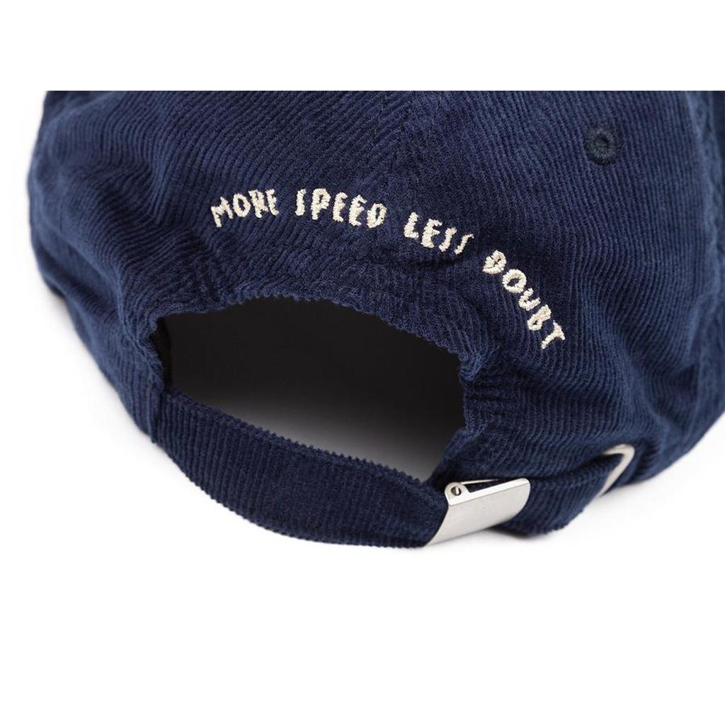 The BSD More Speed Cap is a navy blue corduroy 6-panel hat featuring "MORE SPEED LESS DOUBT" embroidered above the adjustable back strap, blending classic style with a bold message.