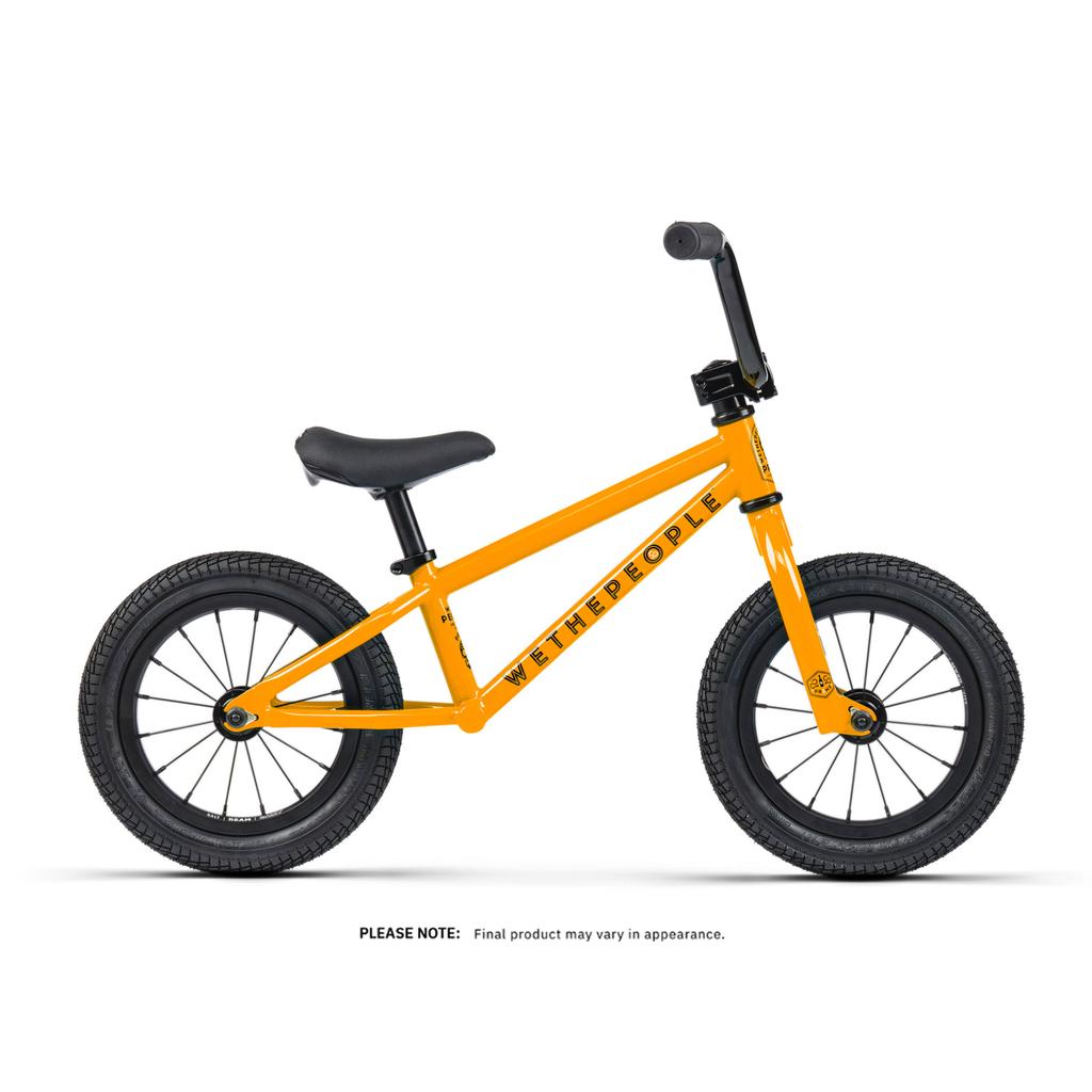 An orange Wethepeople Prime 12 Inch Balance Bike with black wheels, saddle, and handlebars. The BMX-style frame has "WETHEPEOPLE" printed on it.