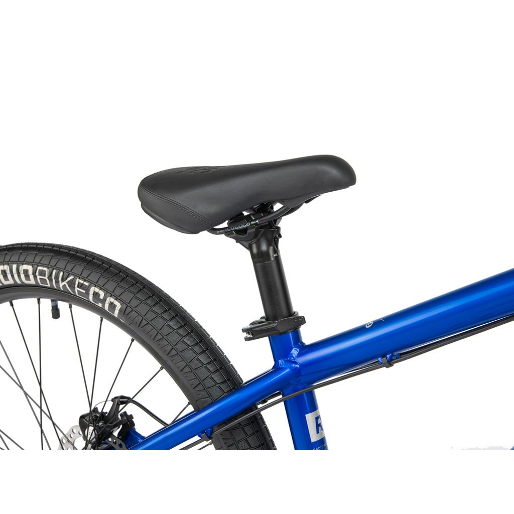 Close-up of the rear section of the Radio Fiend 26 Inch Bike in blue, featuring a black seat and seat post, sturdy 6061-T6 alloy frame, and rear wheel with distinctive tread and white lettering on the tire.
