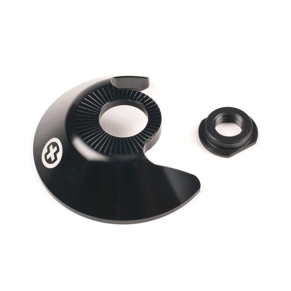 The Saltplus Trapez F/C Hubguard Alloy is a black, semi-circular 7075-T6 metal guard with a grooved inner ring and separate threaded nut, designed for TRAPEZ freecoaster hubs with 14mm axles, shown on a white background.