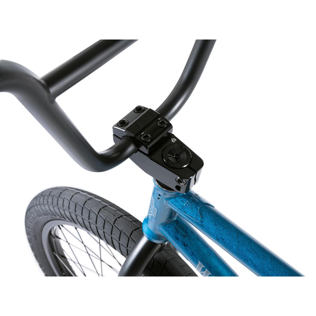 Close-up view of a black handlebar and stem with high-quality aftermarket parts, mounted on a blue Wethepeople Revolver 20 Inch Bike frame with a knobby front tire.