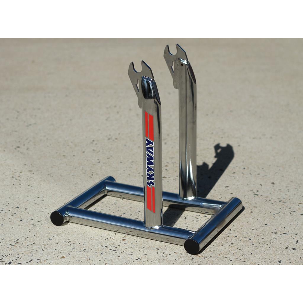 A Skyway Stolz Stand, a chrome bicycle fork stand recalling the Skyway TA Replica BMX stand, stands upright on a sunlit concrete surface.