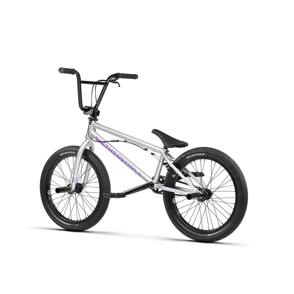 The Wethepeople Versus 20 Inch Bike features a silver frame with "THE COOP" in purple, black handlebars, seat, and tires. Shown on a white background, it’s perfect for skatepark tricks and stunts.
