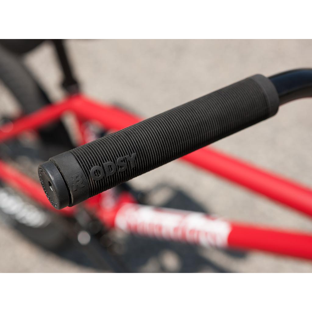 Close-up of a black ribbed handlebar grip with "ODSY" embossed, attached to a red Sunday Forecaster 20 Inch Bike, highlighting quality Odyssey parts.