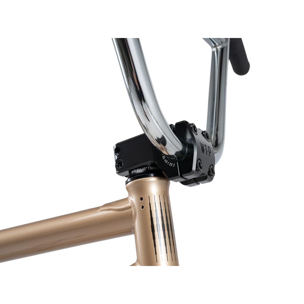 Close-up of the handlebar and stem joined to a metallic gold frame, highlighting the front of the Wethepeople Crysis 20 Inch BMX Bike and its connection points.