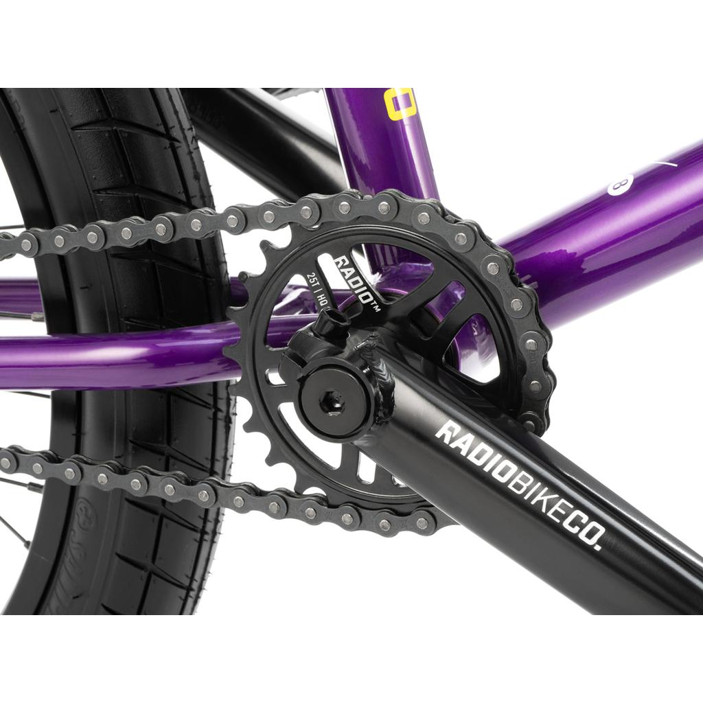 Close-up of a black crankset and chainring on a purple Radio Darko 20 Inch Bike BMX, with part of the rear tire visible.