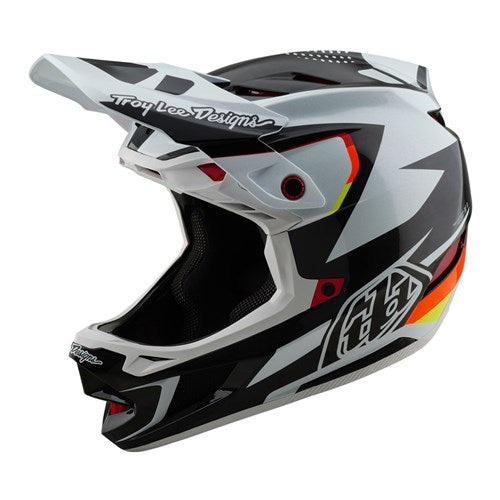 The TLD 25.1 D4 Carbon Helmet (MIPS) in Optic Black showcases striking black, white, and orange angular patterns with the "Troy Lee Designs" logo on top, making it ideal for downhill BMX enthusiasts desiring style and protection.