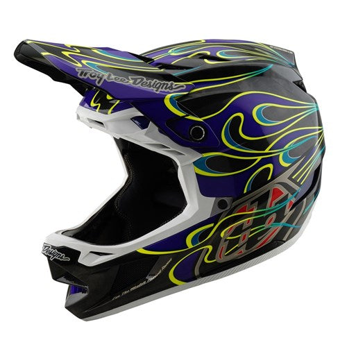 The TLD 25.1 D4 Carbon Helmet (MIPS) in Torched Black/Purple features a vibrant flame design on a sleek carbon fiber base with a prominent visor and aerodynamic shape for enhanced protection.