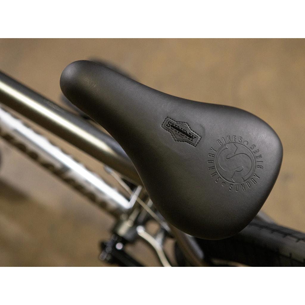 Close-up of a black seat with embossed Sunday branding, mounted on the metallic frame of the Sunday Scout 20 Inch Bike, featuring premium Odyssey components—a signature detail of the Sunday Scout.
